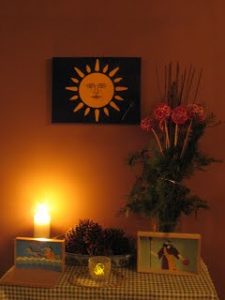 Altar for the solstice, with candles, icon boxes, greenery and a photo of Helios on the wall